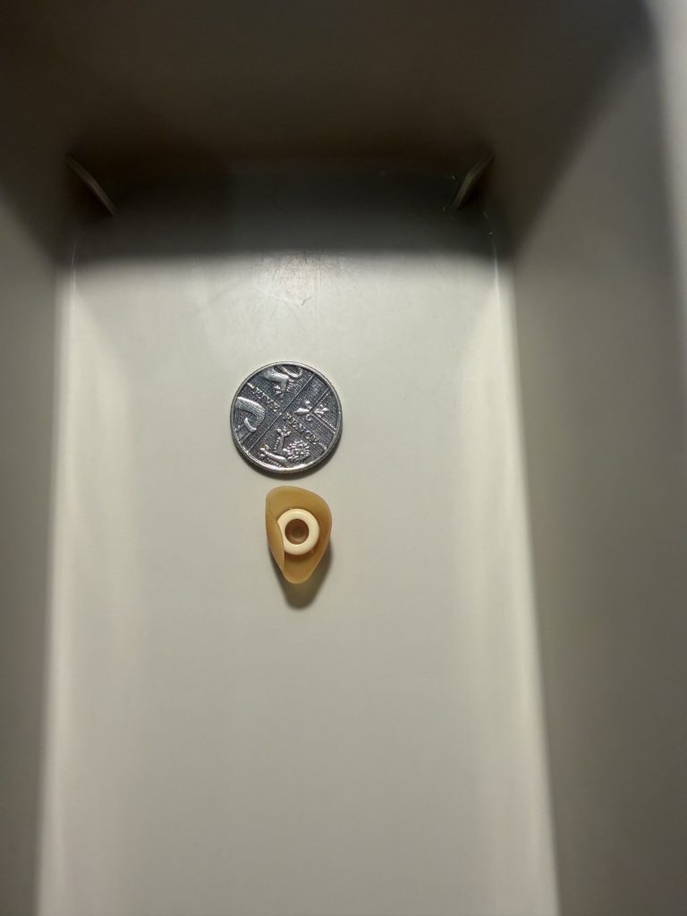 A medium sized earbud from a headphone removed from someone's ear next to a 5 pence piece for scale 